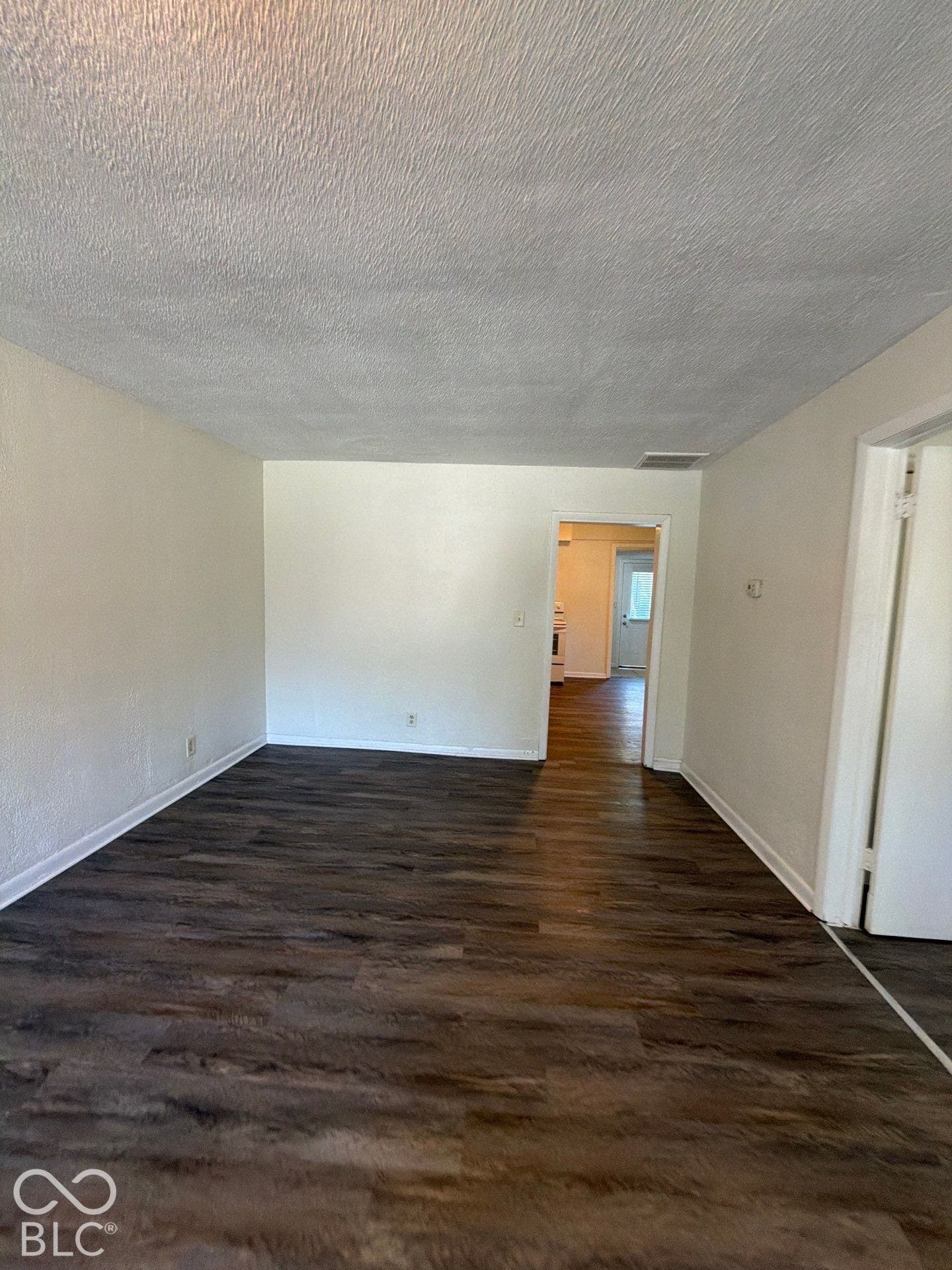 Spacious living area with wood-finish flooring, neutral wall finishes, and abundant natural light