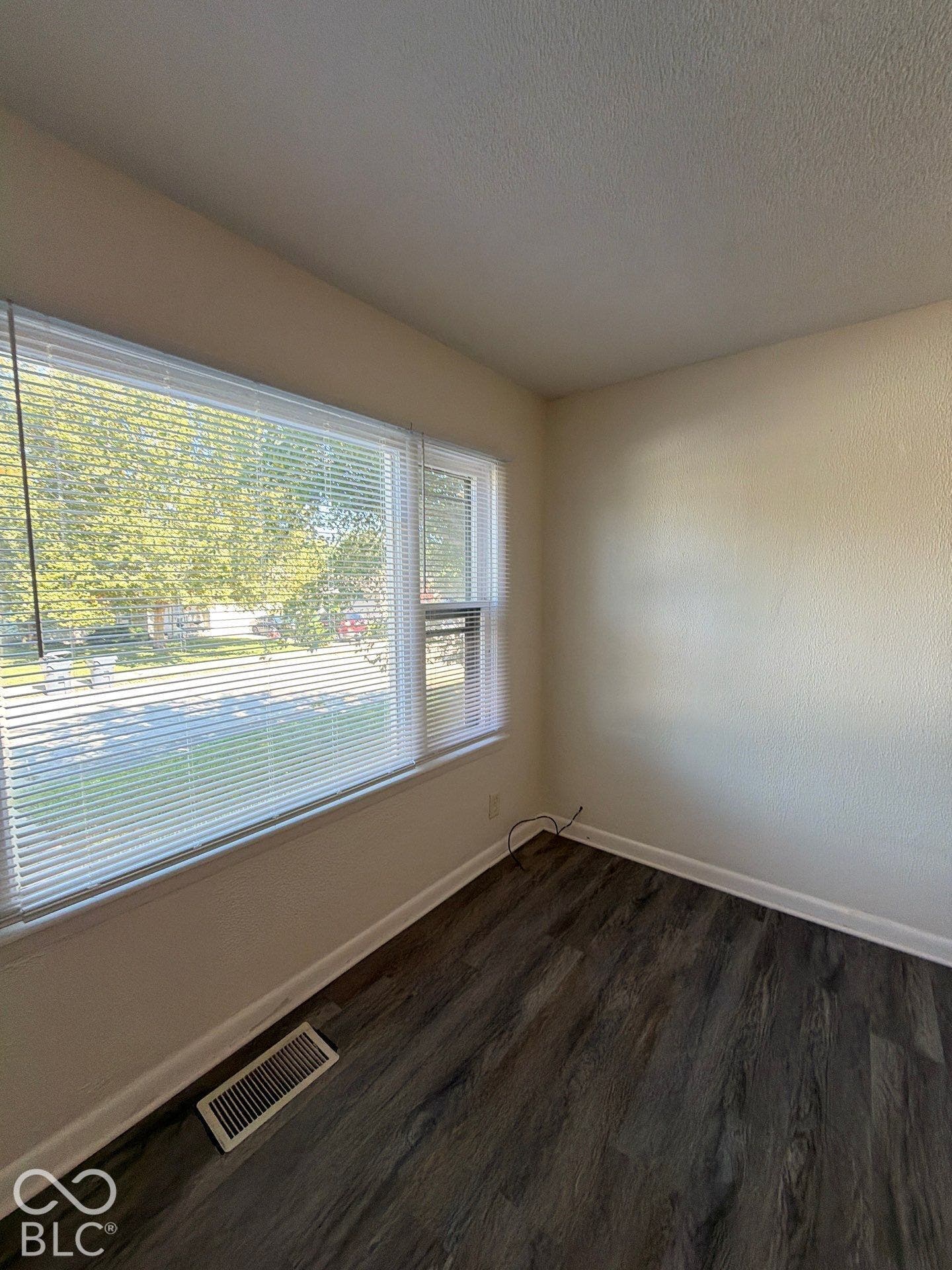 Bright corner room featuring expansive windows with cellular blinds, wood-finish flooring, and fresh neutral walls throughout