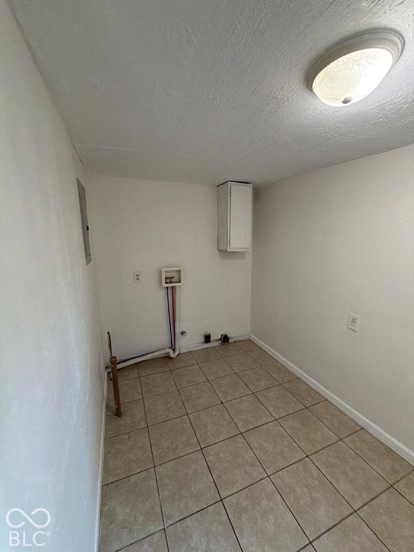 Utility room with tiled flooring, a single wall-mounted cabinet, and an overhead flush-mount light fixture