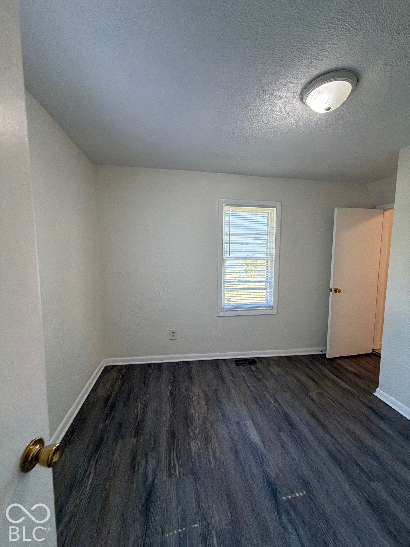 Wood-finish flooring, white painted walls, and a single window with blinds