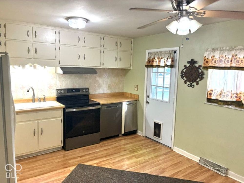 Kitchen featuring wood-laminate finish flooring, white cabinetry, electric range, trash compactor and under-cabinet lighting
