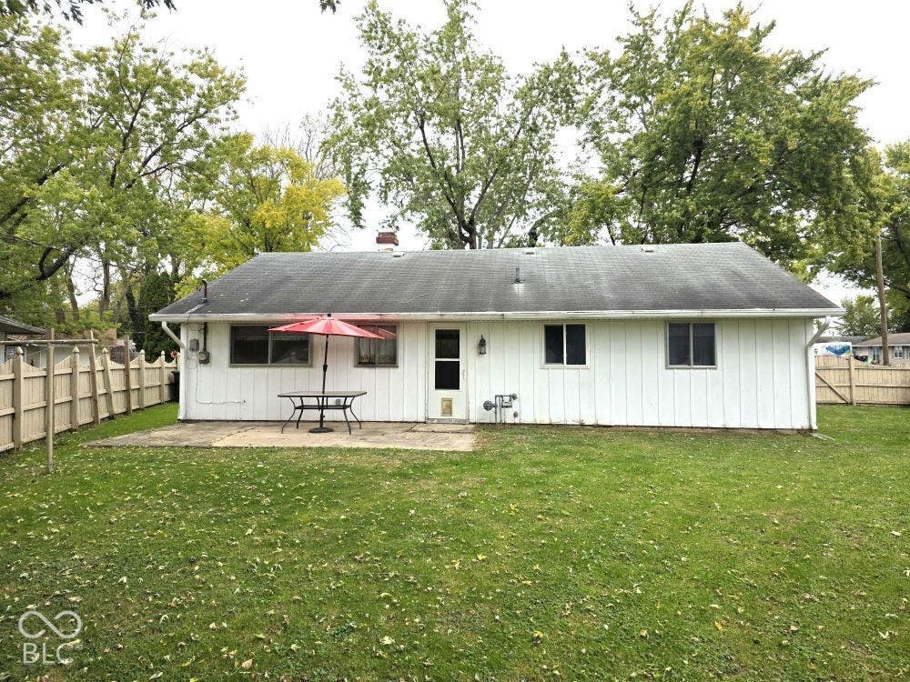 Expansive rear lawn featuring a concrete patio, wood fence, and mature trees