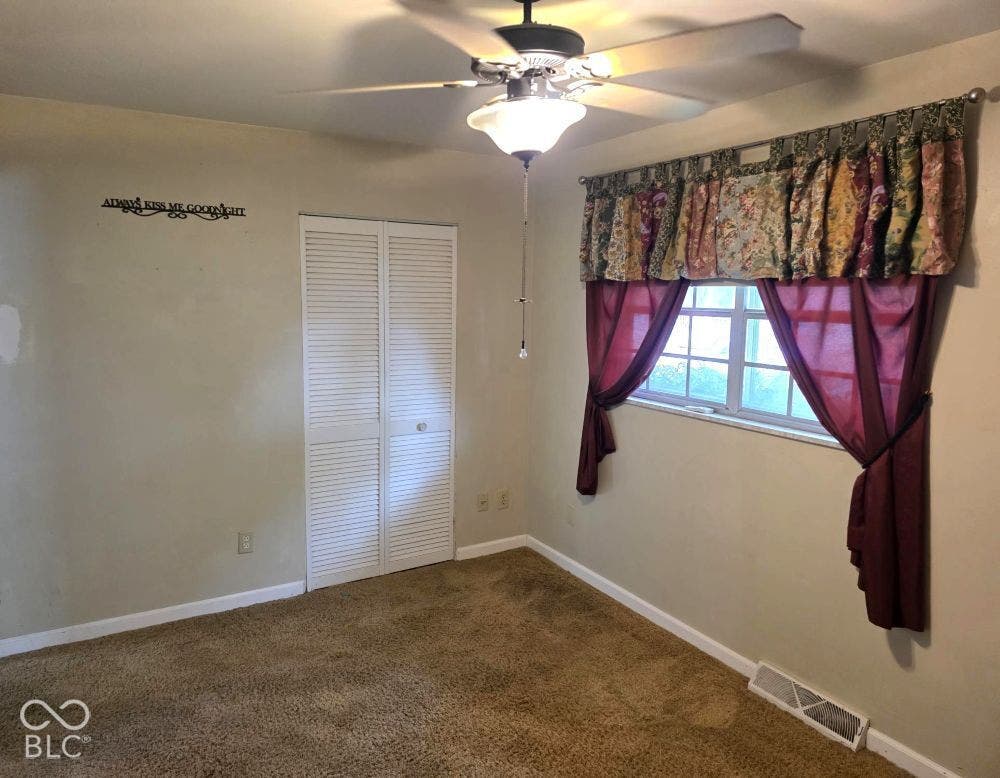 Recessed window with a ceiling fan, louvered bi-fold closet doors, and carpet flooring