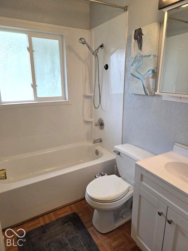 White bathtub with an integrated shower, white framed window, toilet, and a vanity with a white sink