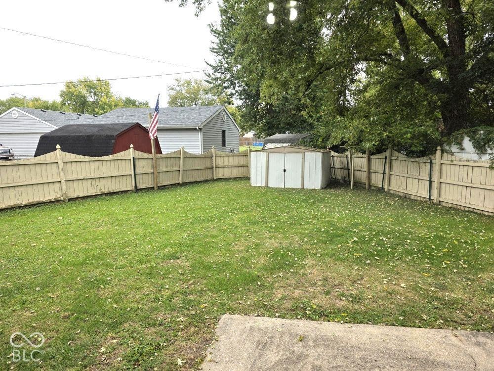 Expansive lawn area, perimeter fencing, storage shed, mature trees, and concrete patio section