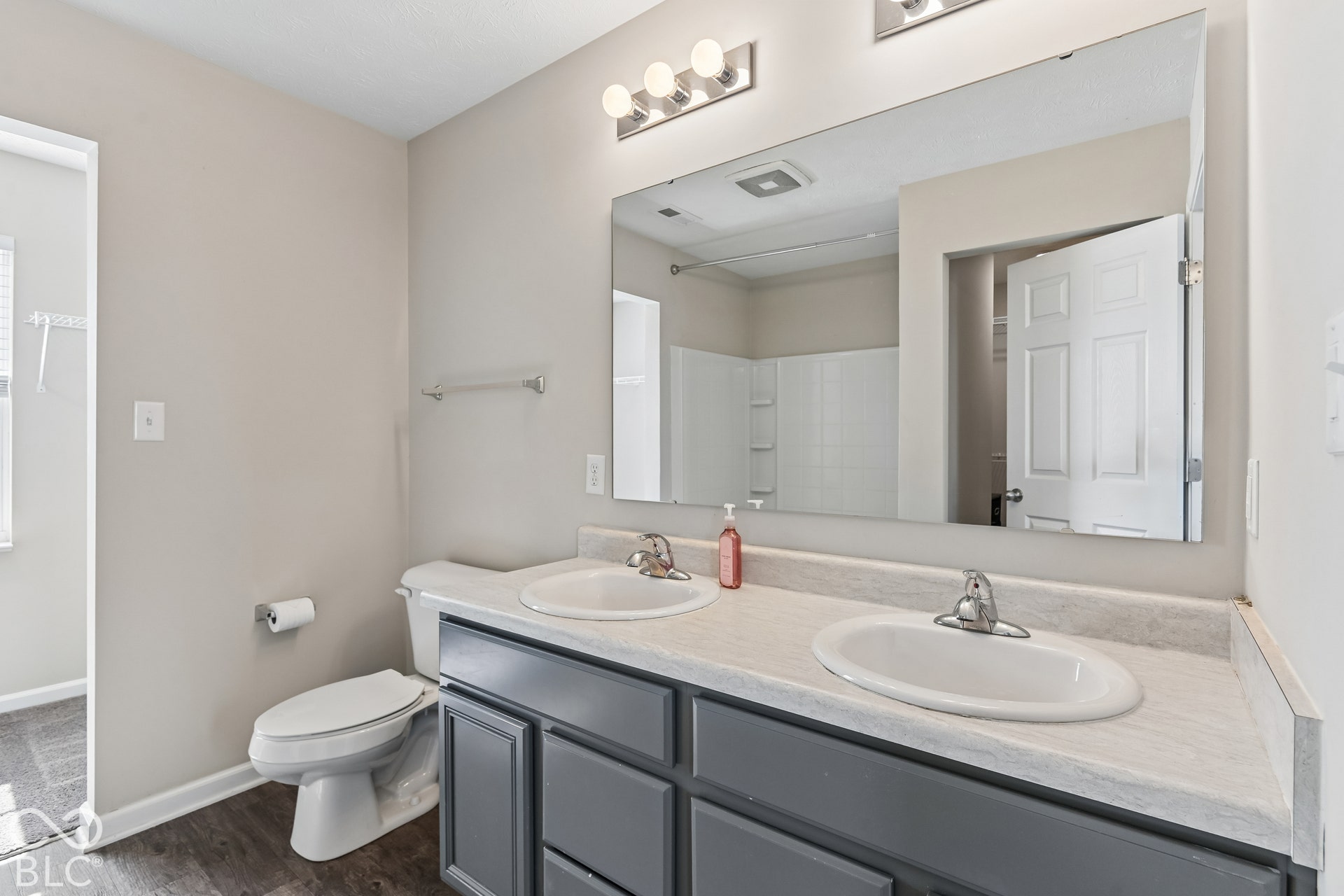 Dual-sink vanity with a neutral solid-surface countertop, dark-toned shaker-style cabinetry, a large wall-mounted mirror, and metallic light fixtures
