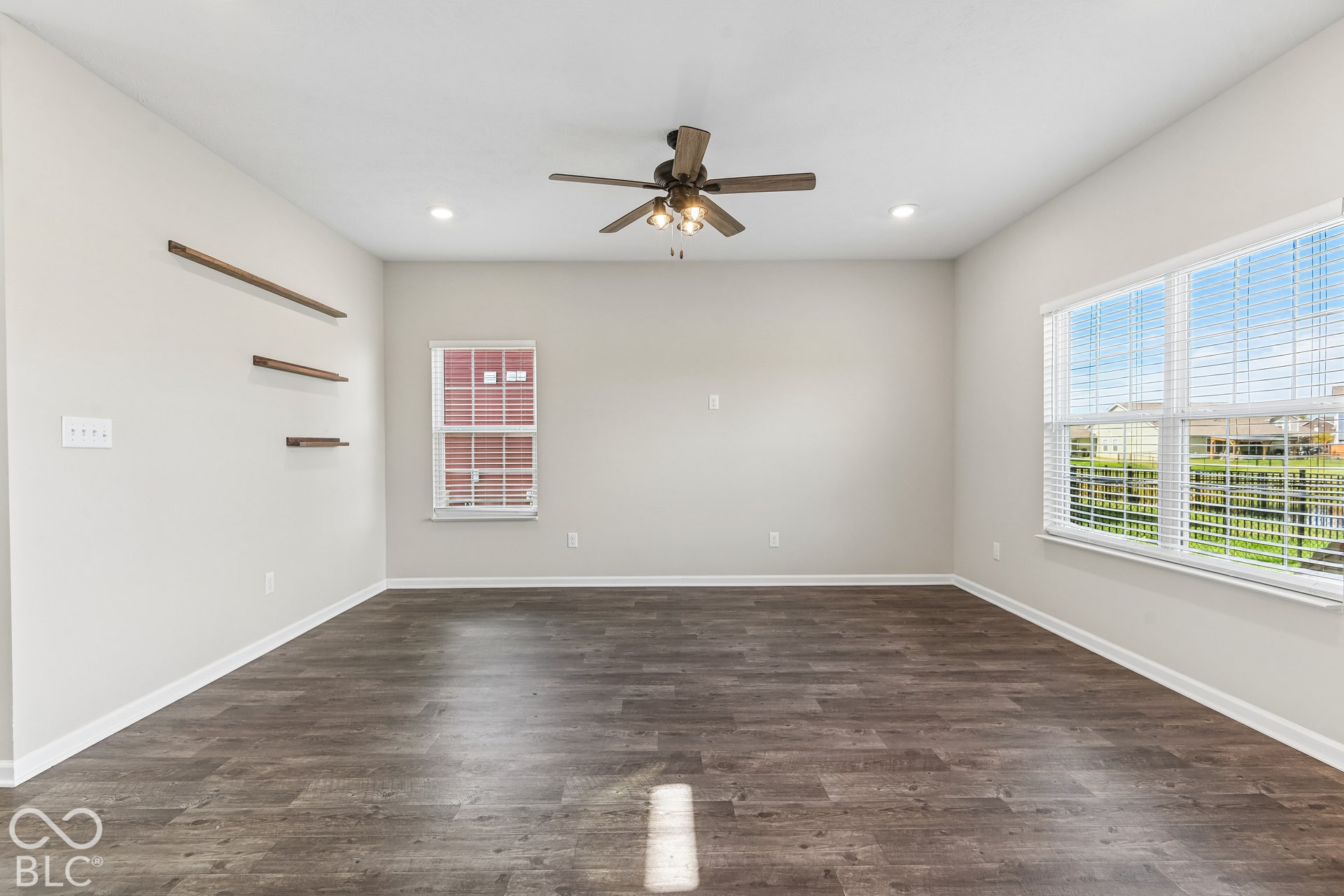 Room featuring vinyl  wood-finish flooring, recessed lighting, a ceiling fan with integrated light fixture, horizontal wall-mounted shelving, and large windows with blinds