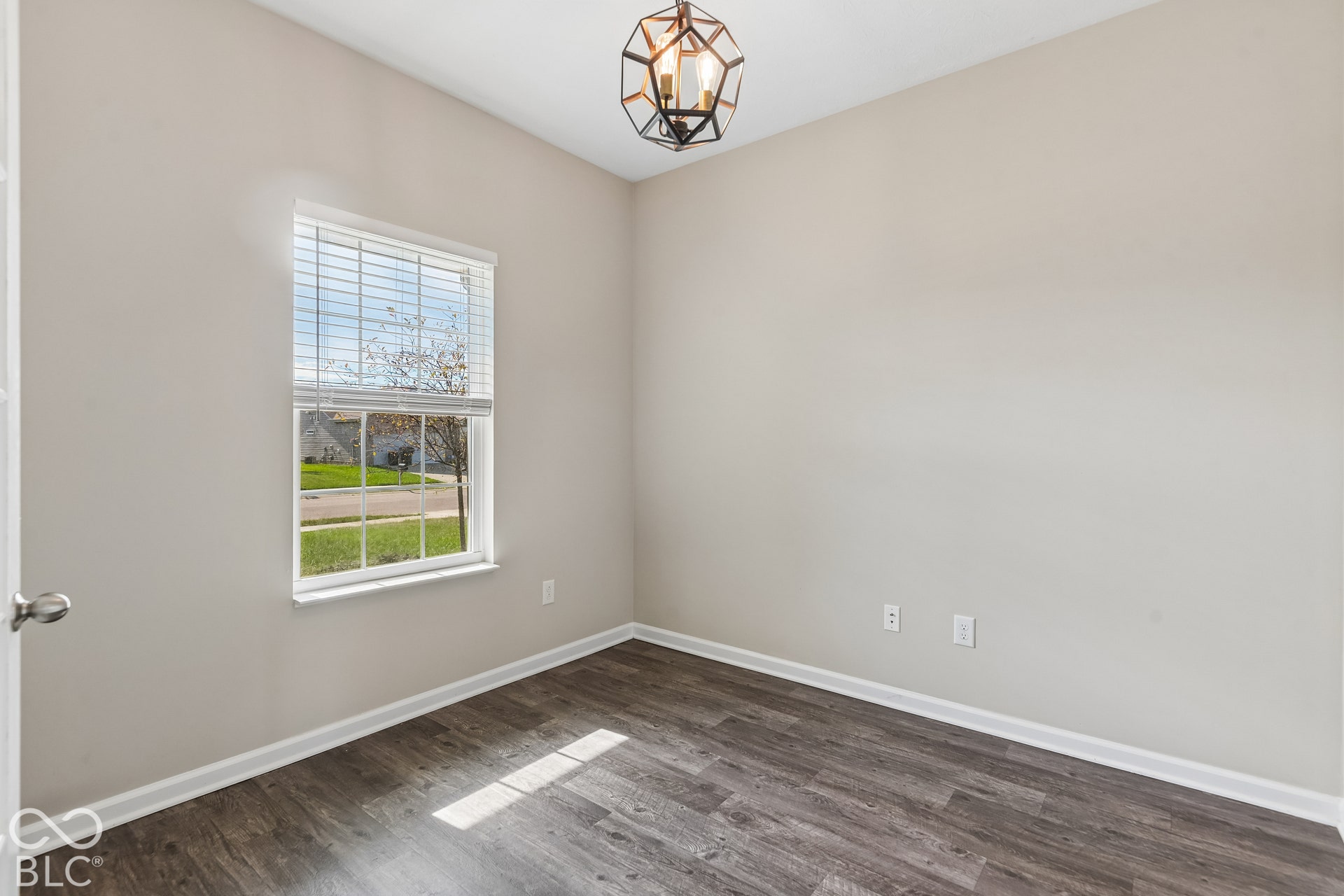 Room featuring vinyl wood-finish flooring, a single-pane window with interior blinds, and a geometric metal pendant light fixture