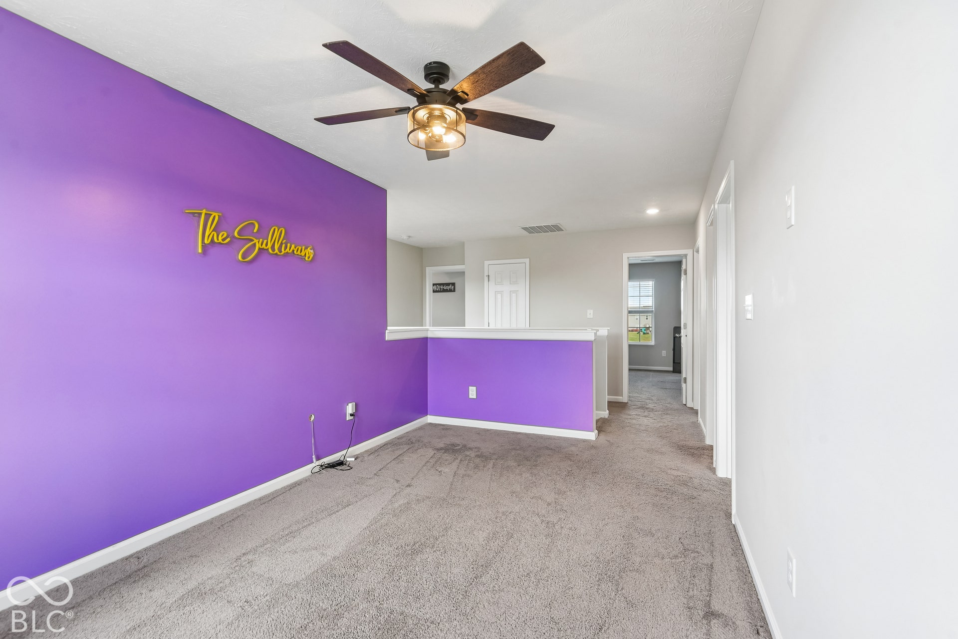 Neutral carpeting, ceiling fan with integrated lighting, and painted accent wall