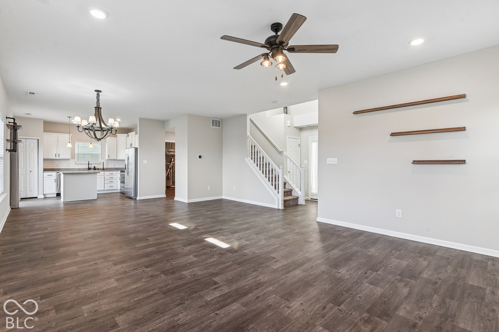 Open-concept interior featuring vinyl  wood-finish flooring, a ceiling fan with integrated lighting, built-in wall shelving, a staircase with white balusters, and a kitchen island with white cabinetry