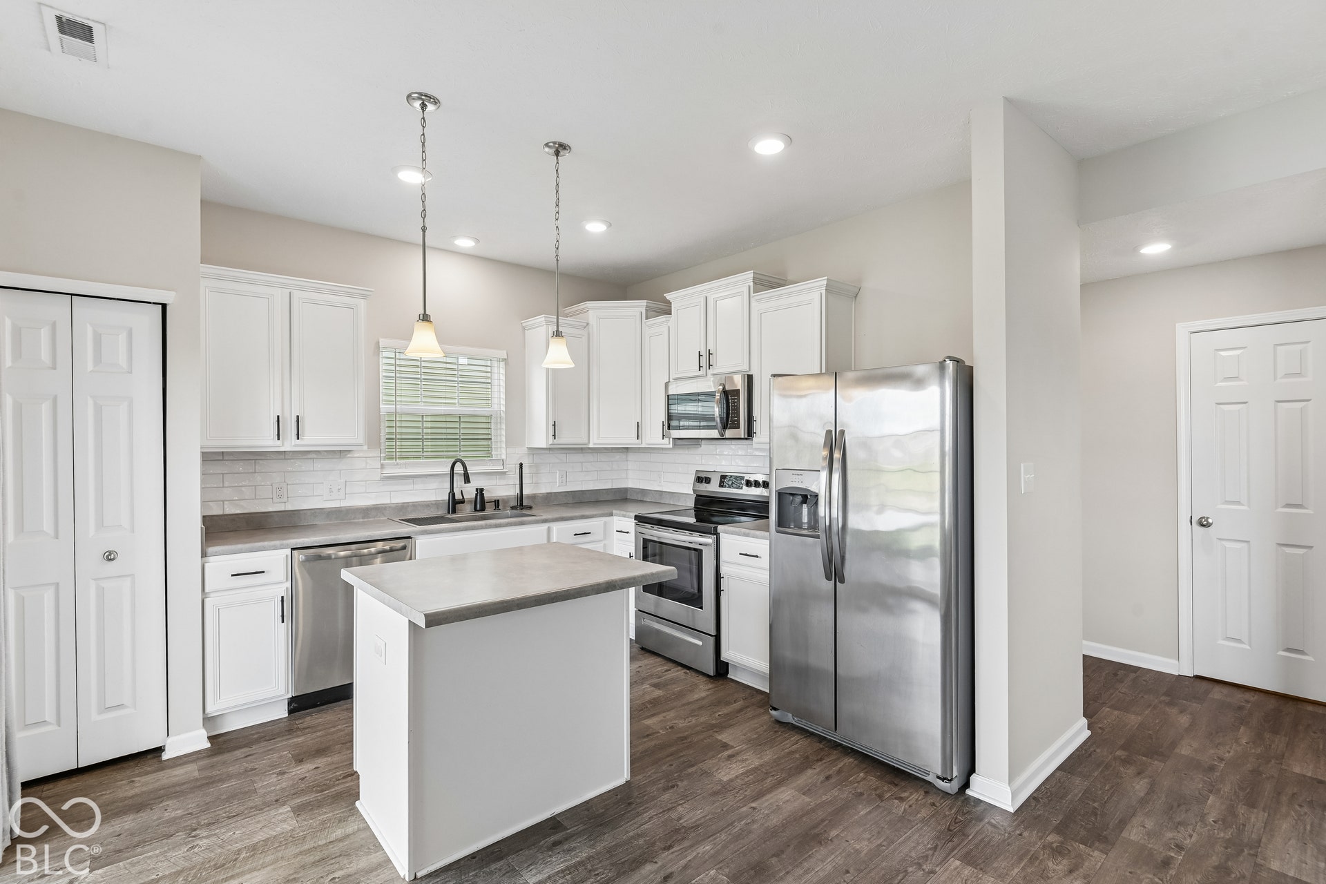 Kitchen featuring white cabinetry, subway tile backsplash, center island, stainless steel appliances, and vinyl wood-finish flooring