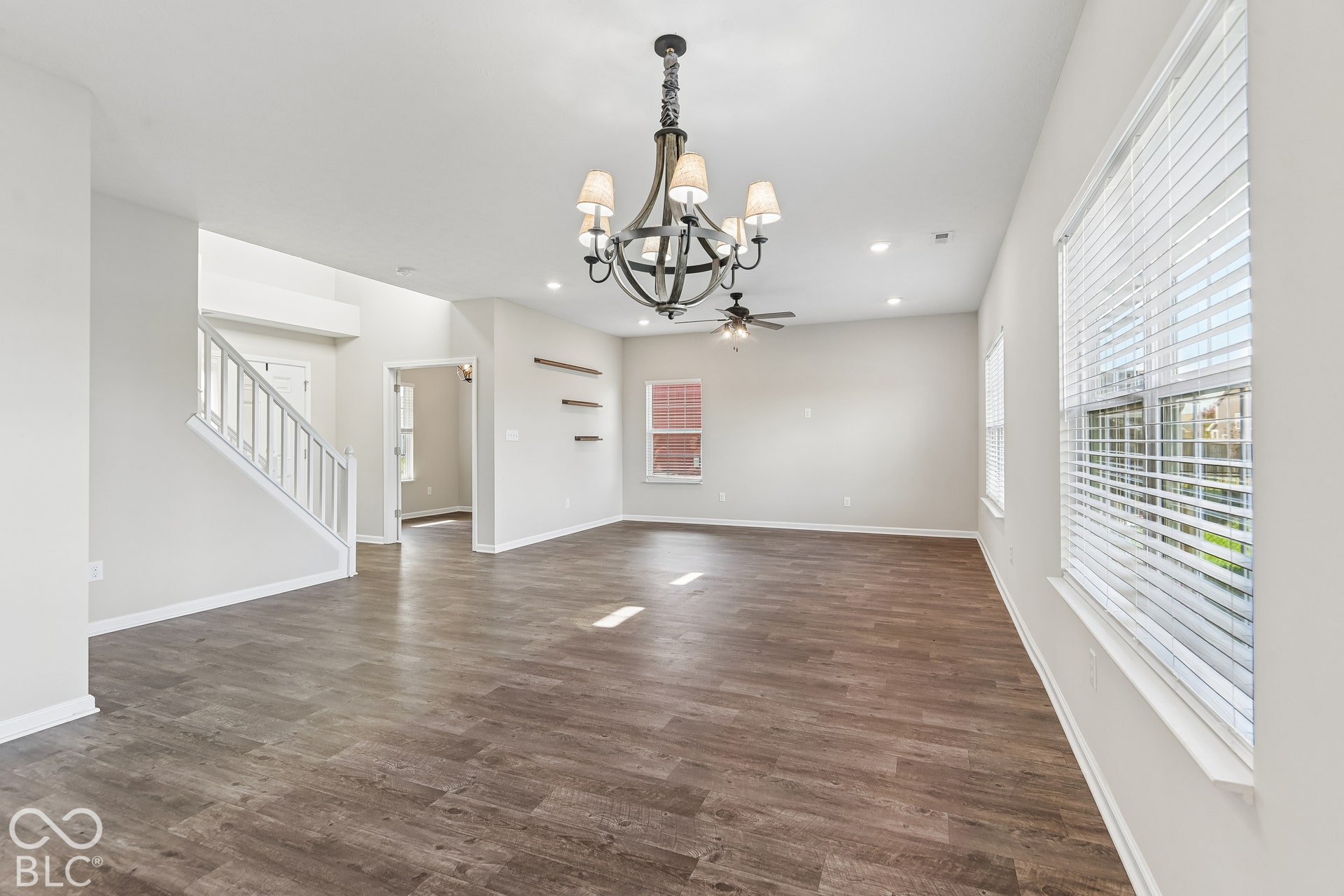 Open-concept interior featuring wood-finish flooring, a multi-arm candelabra-style chandelier, recessed lighting, built-in wall shelving, and a white wooden staircase railing