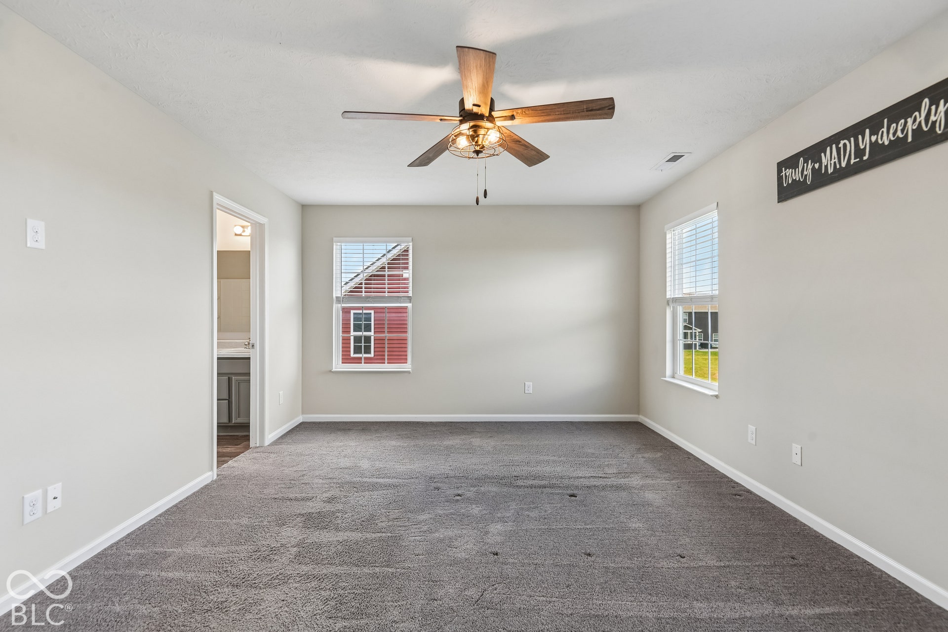 Neutral-toned interior space featuring neutral carpeting, double-hung windows, and a ceiling fan with integrated lighting