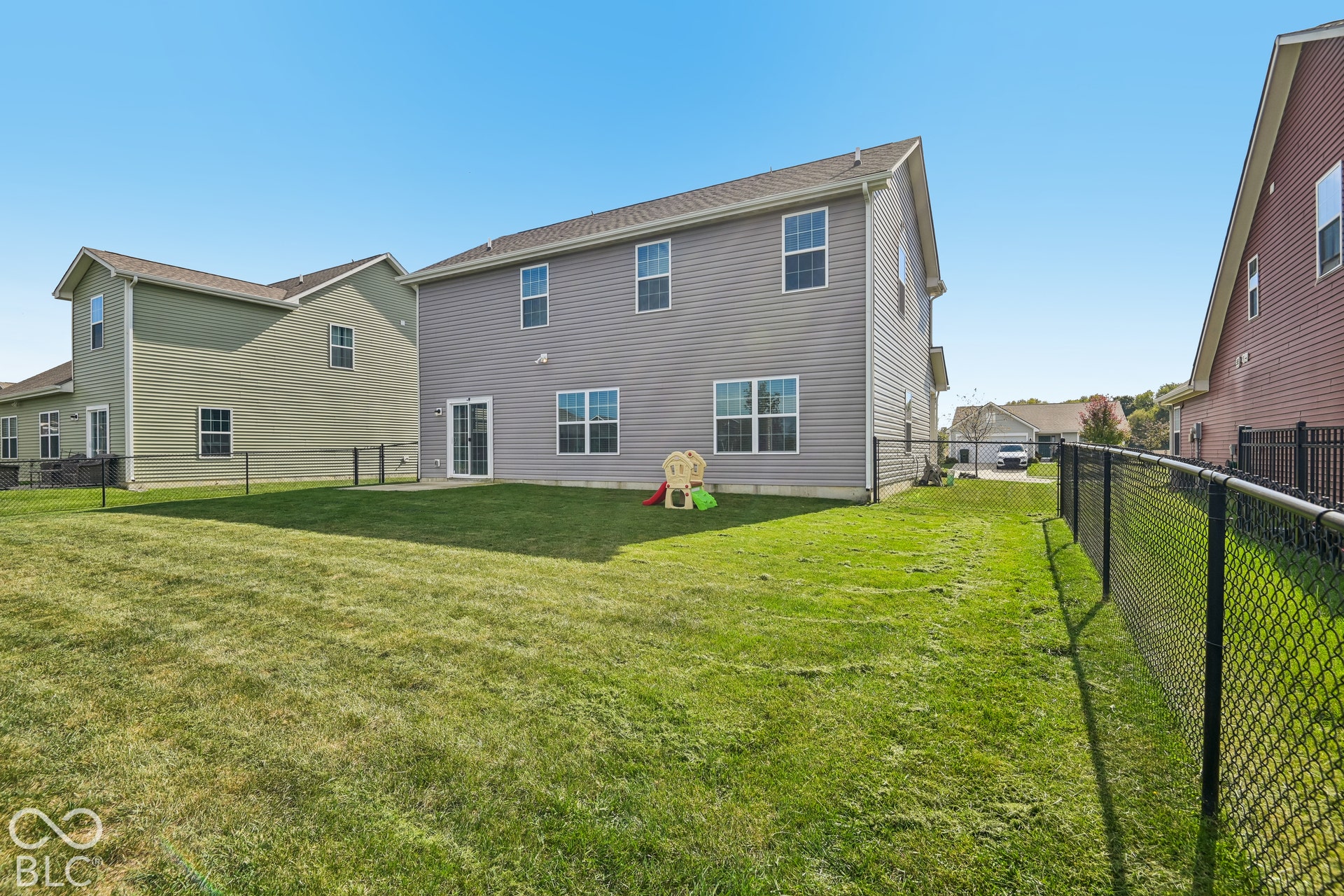 Rear exterior featuring horizontal vinyl siding, multi-pane windows, a sliding glass door, and a fenced backyard with a concrete patio