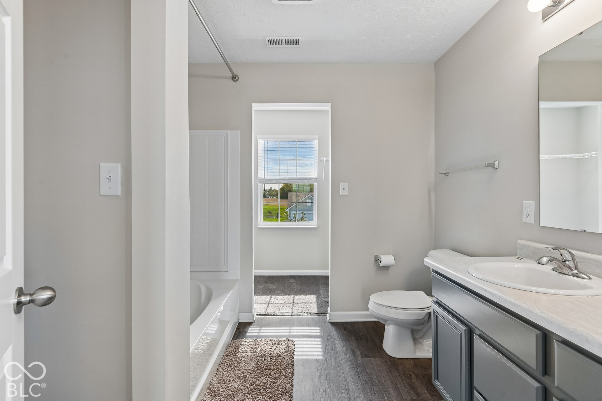 Bathroom featuring a vanity with gray cabinetry, a white integrated sink countertop, a wall-mounted mirror, vinyl  wood-finish flooring, and a shower-tub combination with a white surround