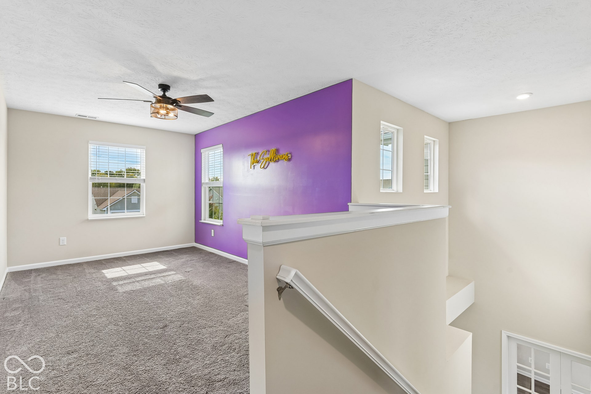 Open Loft area featuring wall-to-wall carpeting, ceiling fan with integrated lighting, accent wall, and multiple double-hung windows perfect for a play or game area