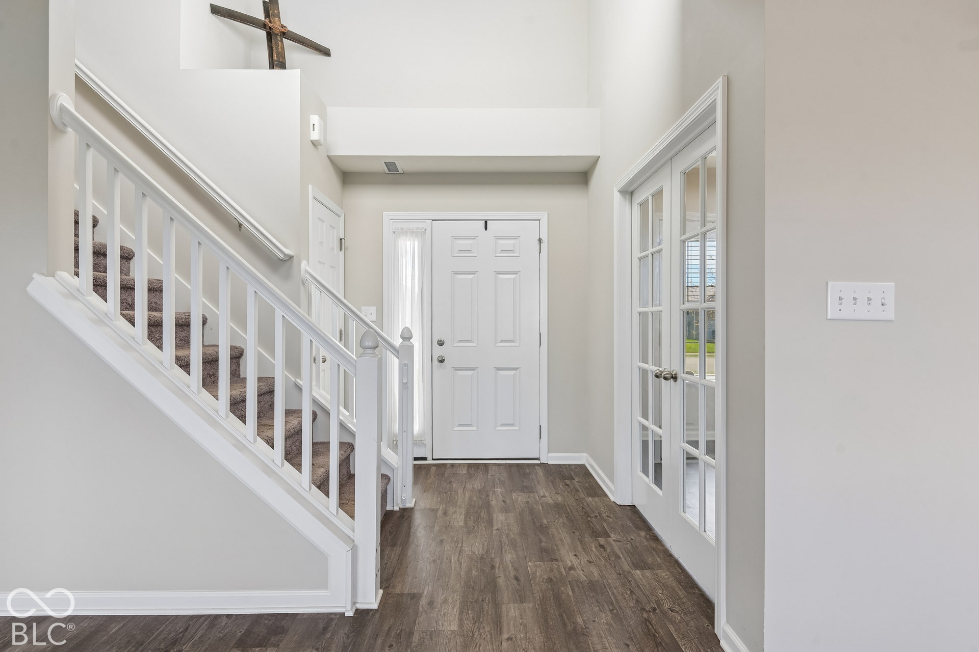 Entryway featuring high ceilings, vinyl wood-finish flooring, a white staircase with balusters, and French doors with glass panes