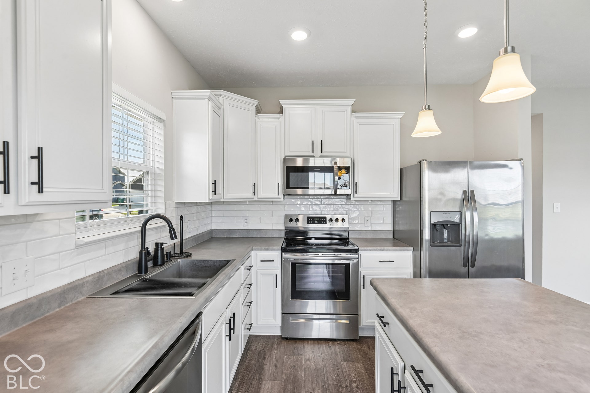Kitchen featuring white shaker-style cabinetry, matte-finish countertops, subway tile backsplash, stainless steel appliances, and vinyl  wood-finish flooring