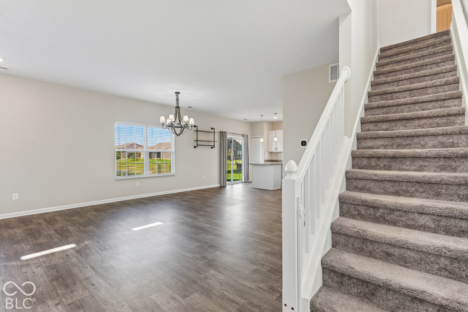 Open-concept interior featuring vinyl  wood-finish flooring, a multi-light metal chandelier, carpeted staircase with white balusters, and sliding glass doors