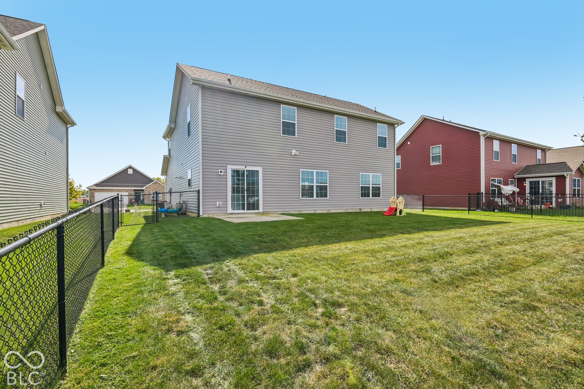 Rear exterior featuring horizontal vinyl siding, a concrete patio, and a fully enclosed chain-link fenced yard