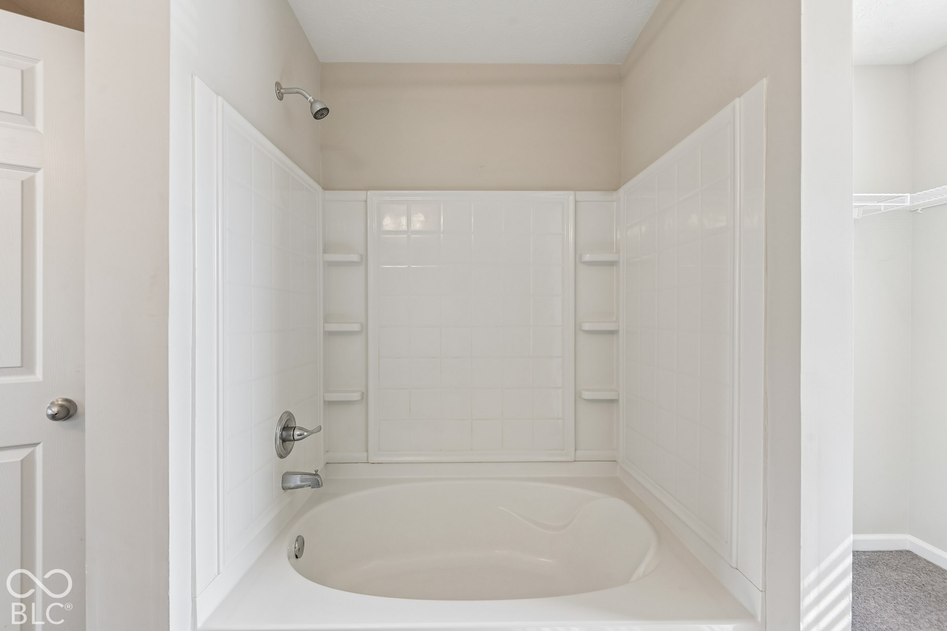 Built-in soaking tub with a tiled surround, integrated shelving, and a chrome shower fixture