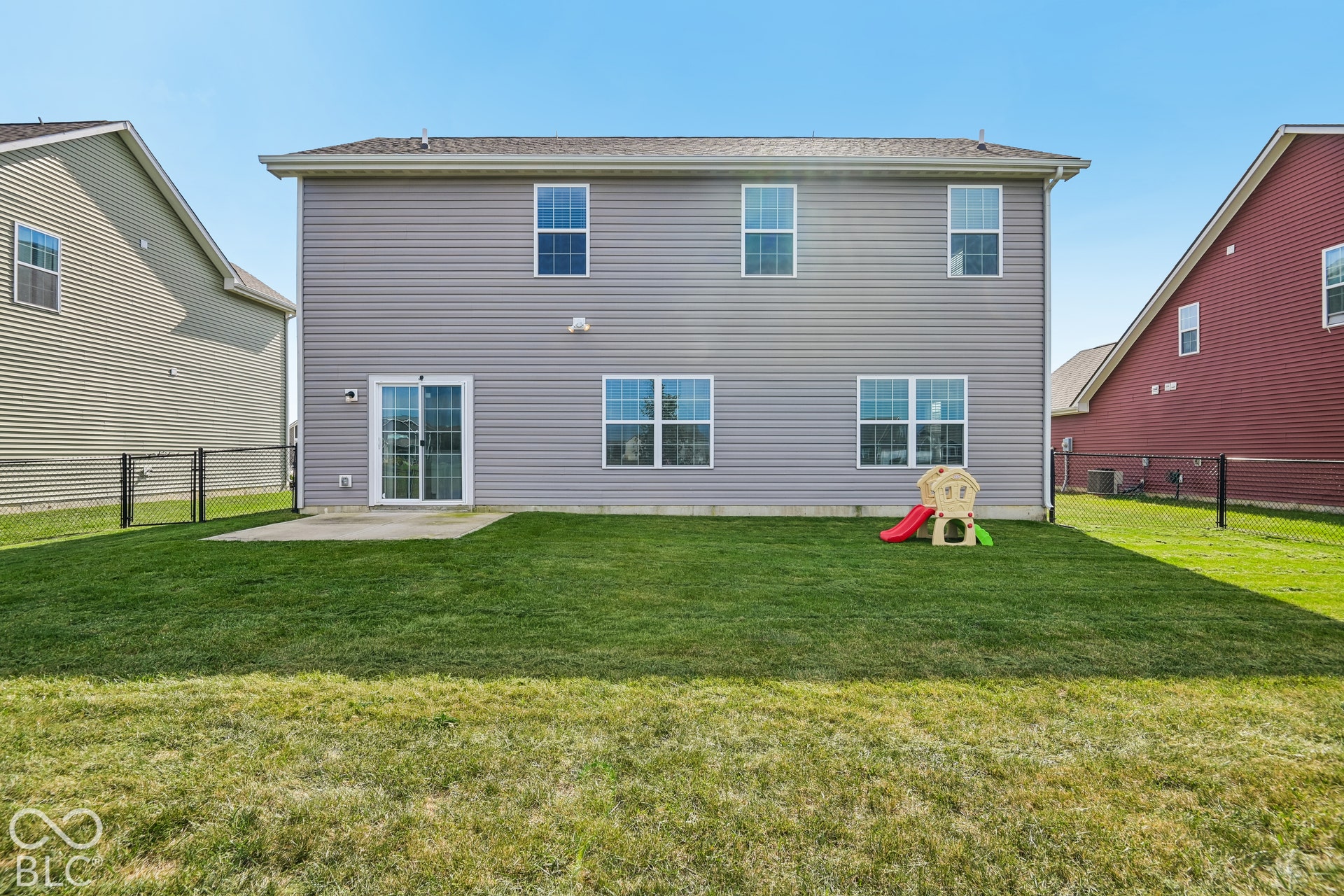 Rear exterior featuring light-gray horizontal siding, multi-pane windows, sliding glass door, concrete patio, and fenced backyard