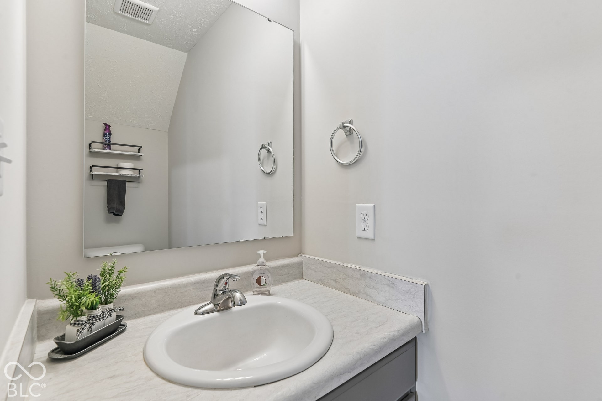 Vanity featuring a stone-finish countertop with an integrated basin, chrome finish faucet, large frameless wall-mounted mirror, and wall-mounted metal towel ring