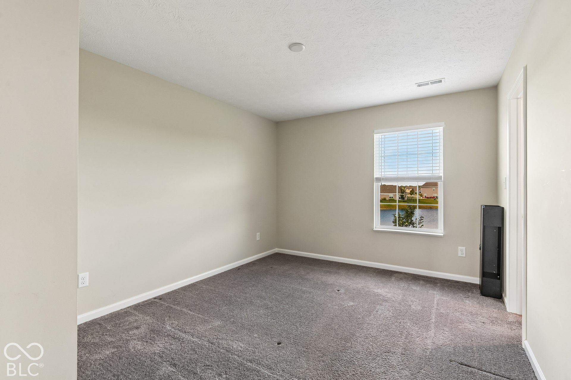 Neutral-toned interior space featuring wall-to-wall carpeting, a single-pane window with blinds, and exterior water scenery