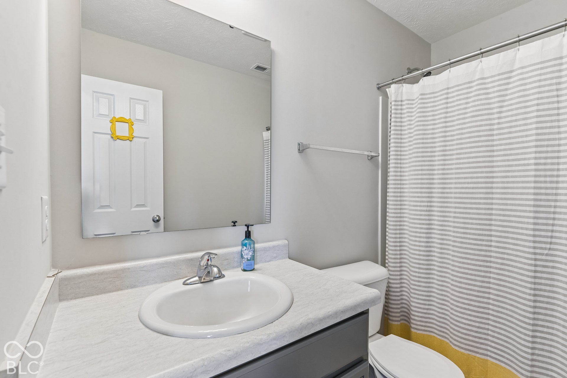 Bathroom featuring a solid-surface countertop with an integrated basin, large wall-mounted mirror, and a neutral-toned vanity cabinet