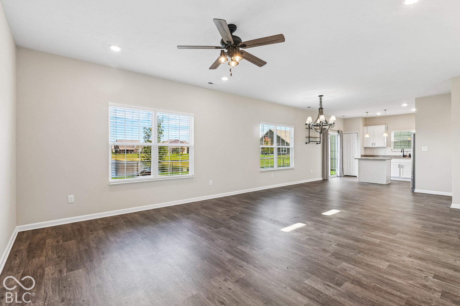 Open interior featuring vinyl wood flooring, recessed lighting, ceiling fan with integrated lighting, multiple windows, and a kitchen island with pendant lighting