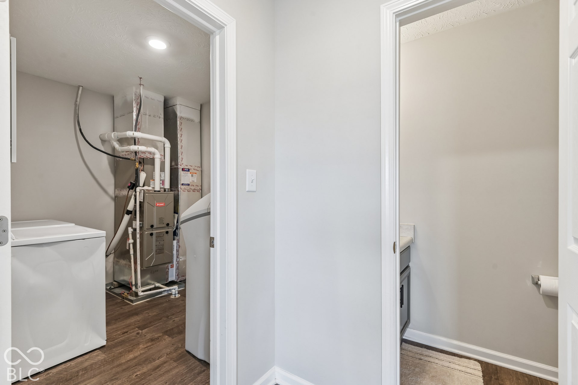 Utility room featuring wood-finish flooring, a metal furnace unit, and white plumbing fixtures, water softener included