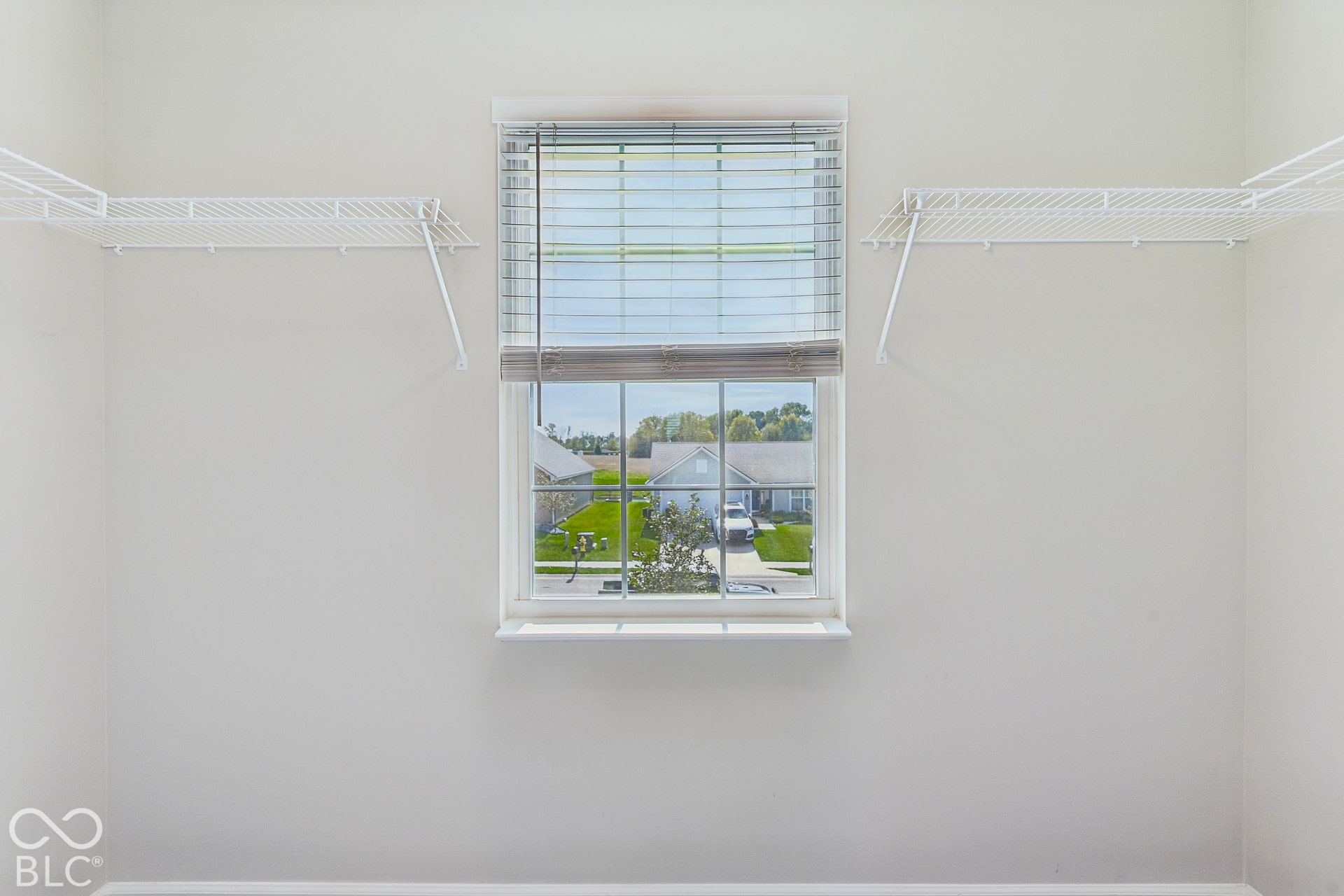 Storage space featuring dual wall-mounted white wire shelving units and a central window with multi-pane glazing and horizontal blinds