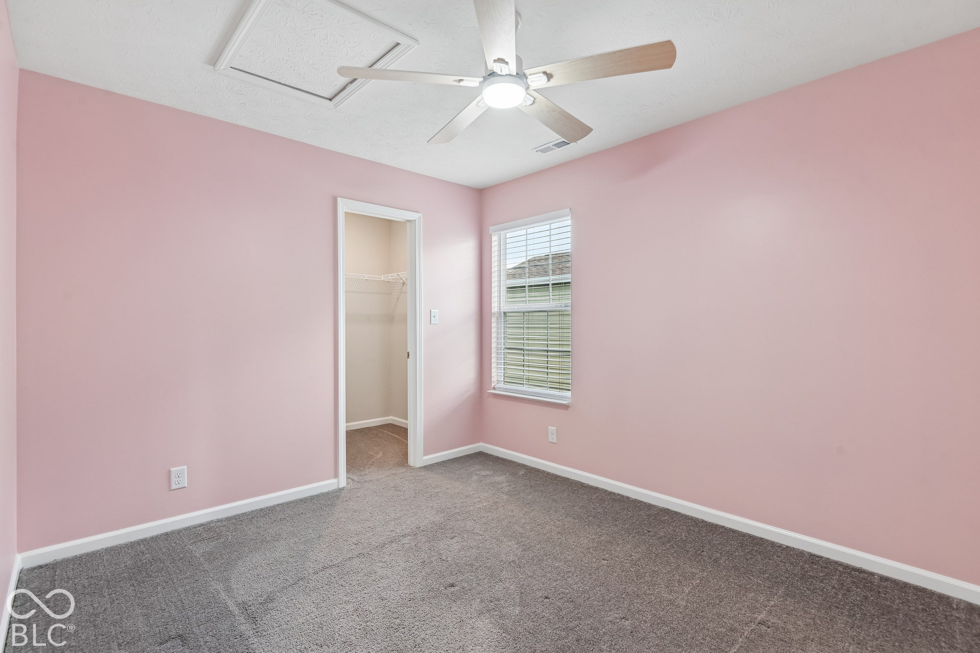 Room featuring neutral carpeting, a central ceiling fan with integrated lighting, a single window, and a walk-in closet