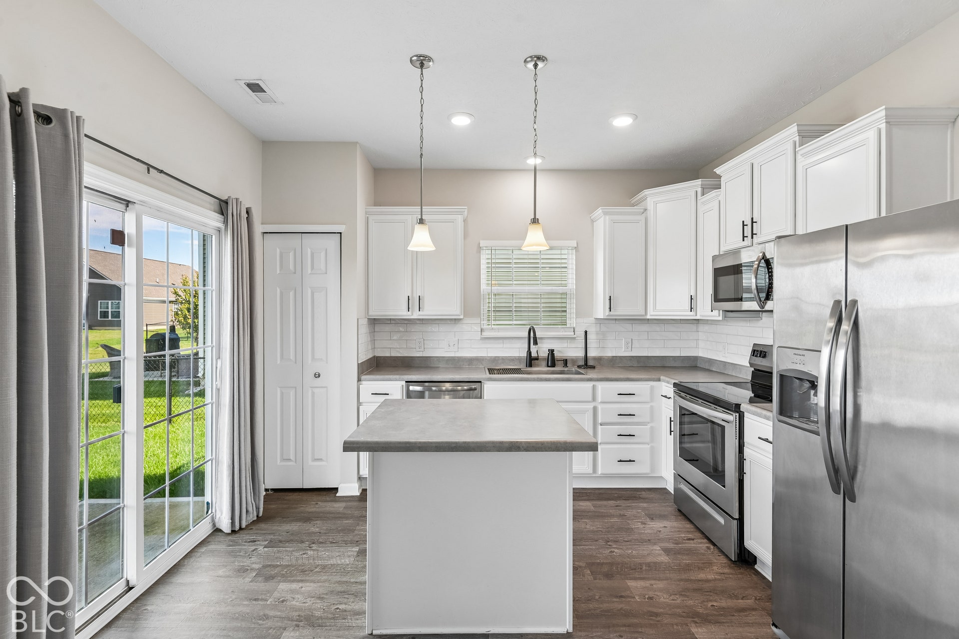 Kitchen featuring white shaker-style cabinetry, an island with a countertop, stainless steel appliances, subway tile backsplash, and vinyl wood-finish flooring