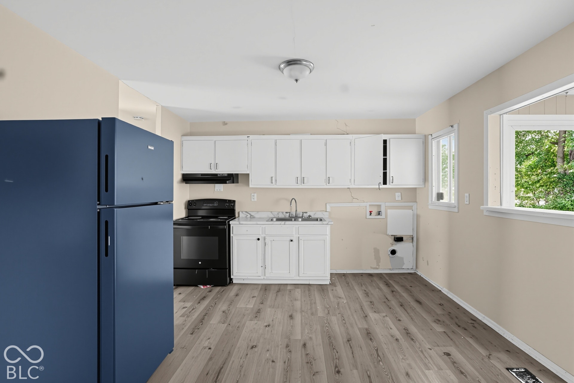 Kitchen featuring white cabinetry, wood-finish flooring, a stainless steel dual-basin sink, and a black range