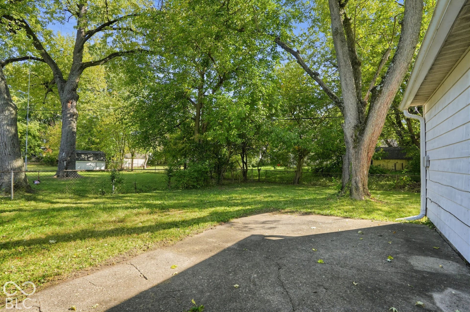Backyard featuring a concrete patio, mature trees, and an expansive lawn area
