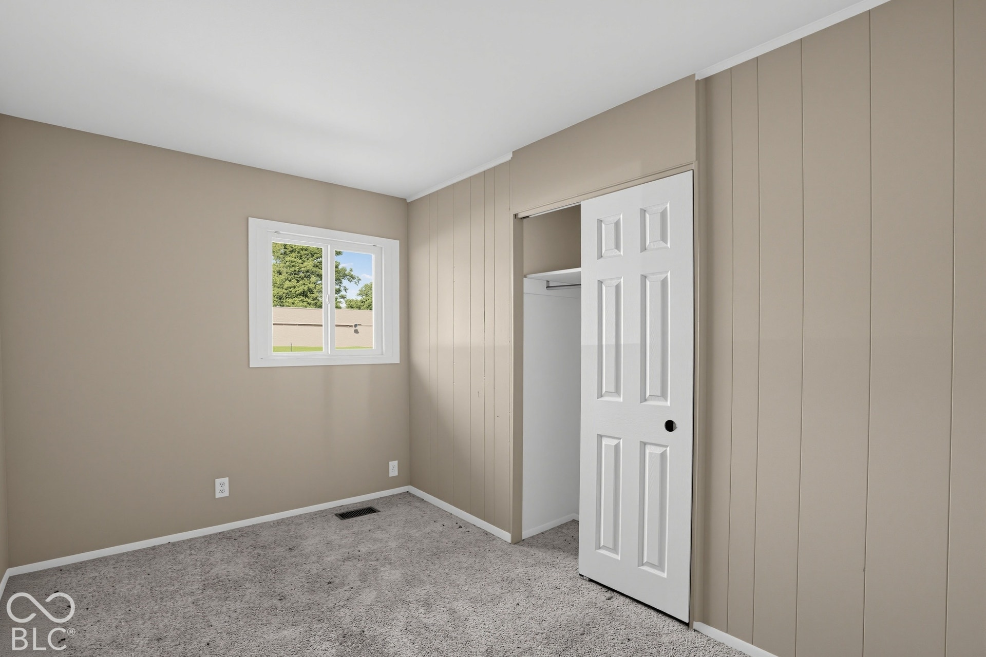 Interior space featuring vertical wood-paneled walls, carpeted flooring, a white-framed window, and a closet with a six-panel door