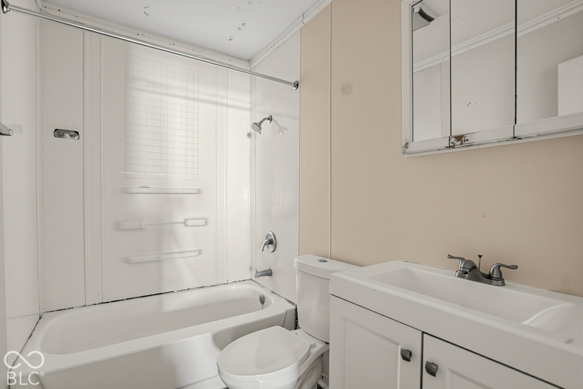 Bathroom featuring a white vanity cabinet, integrated sink, mirrored medicine cabinet, and a combined tub and shower surround with built-in shelving