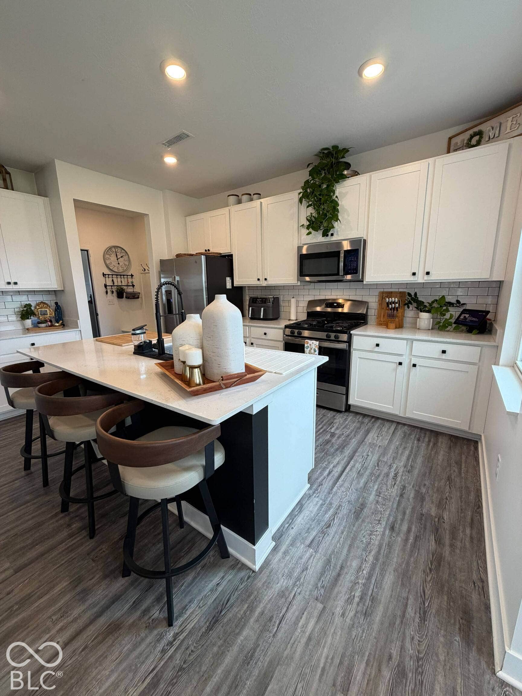 Kitchen featuring a central island with countertop seating, white cabinetry, stainless steel appliances, a white subway tile backsplash, and wood-finish flooring