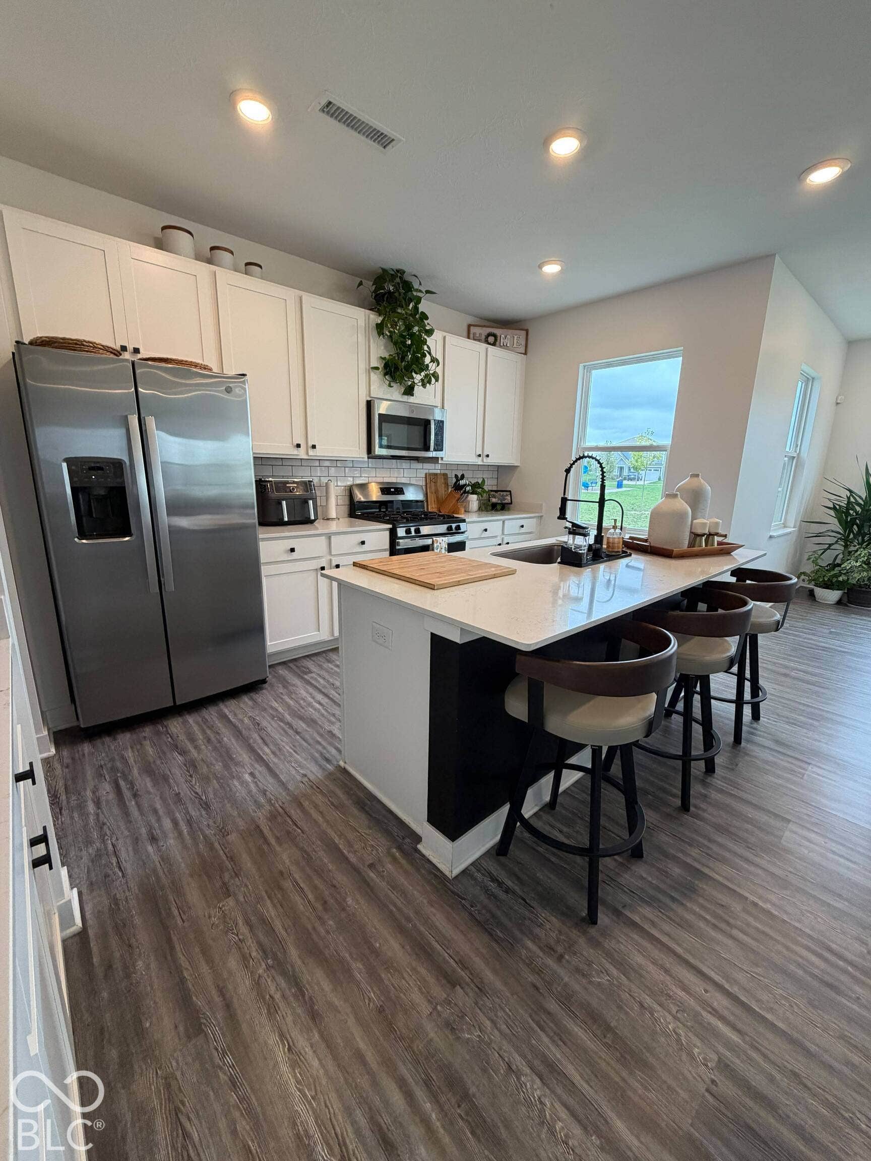 Kitchen featuring white cabinetry, stainless steel appliances, a center island with countertop seating, wood-finish flooring, and recessed lighting