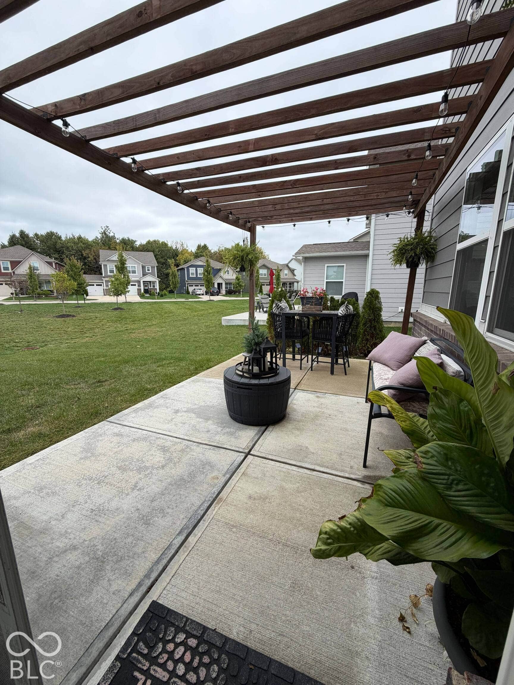 Expansive concrete patio with a wooden pergola, string lighting, and direct access to a large lawn