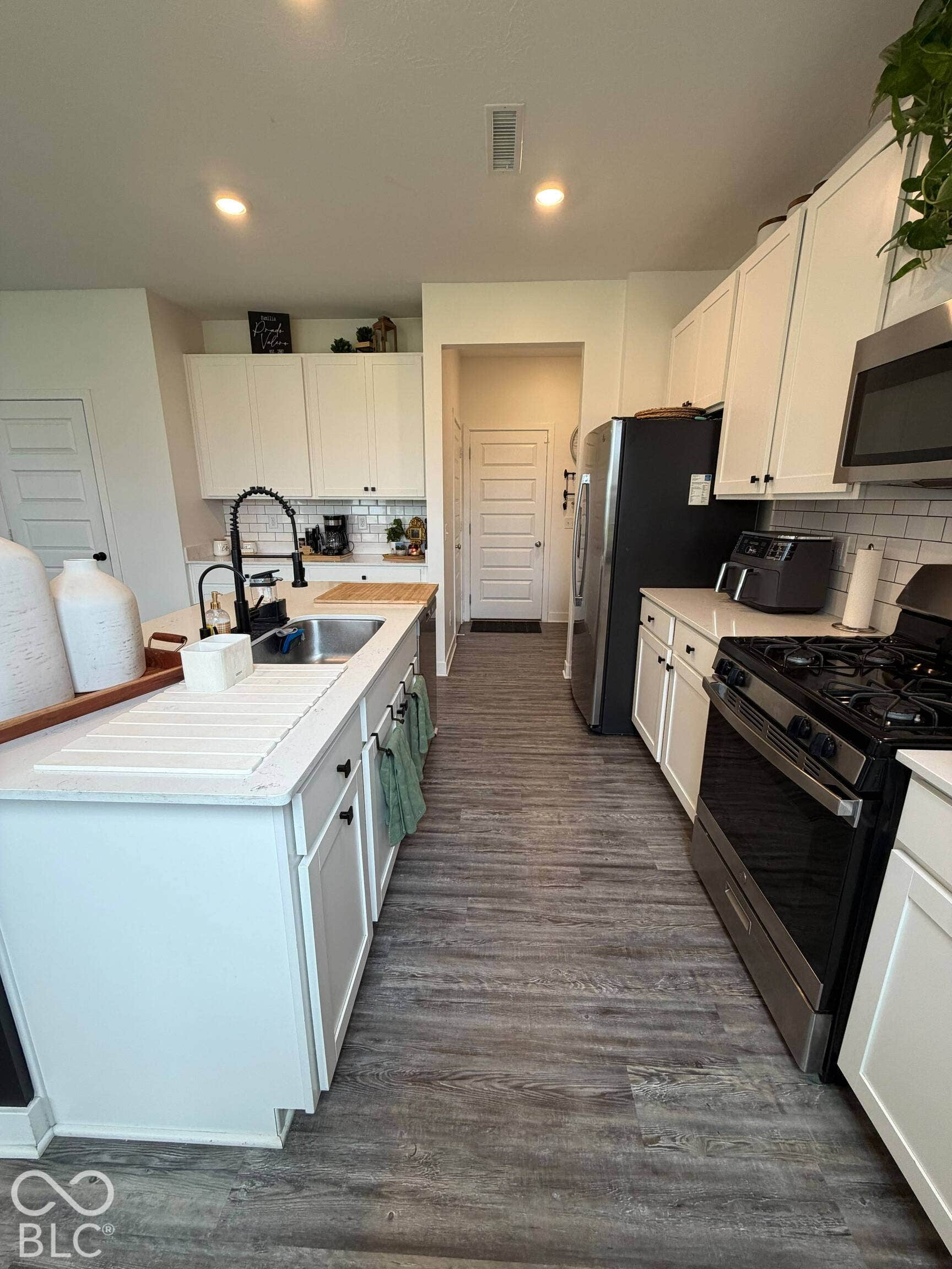 Wood-finish flooring, white cabinetry, stainless steel appliances, subway tile backsplash, and recessed lighting