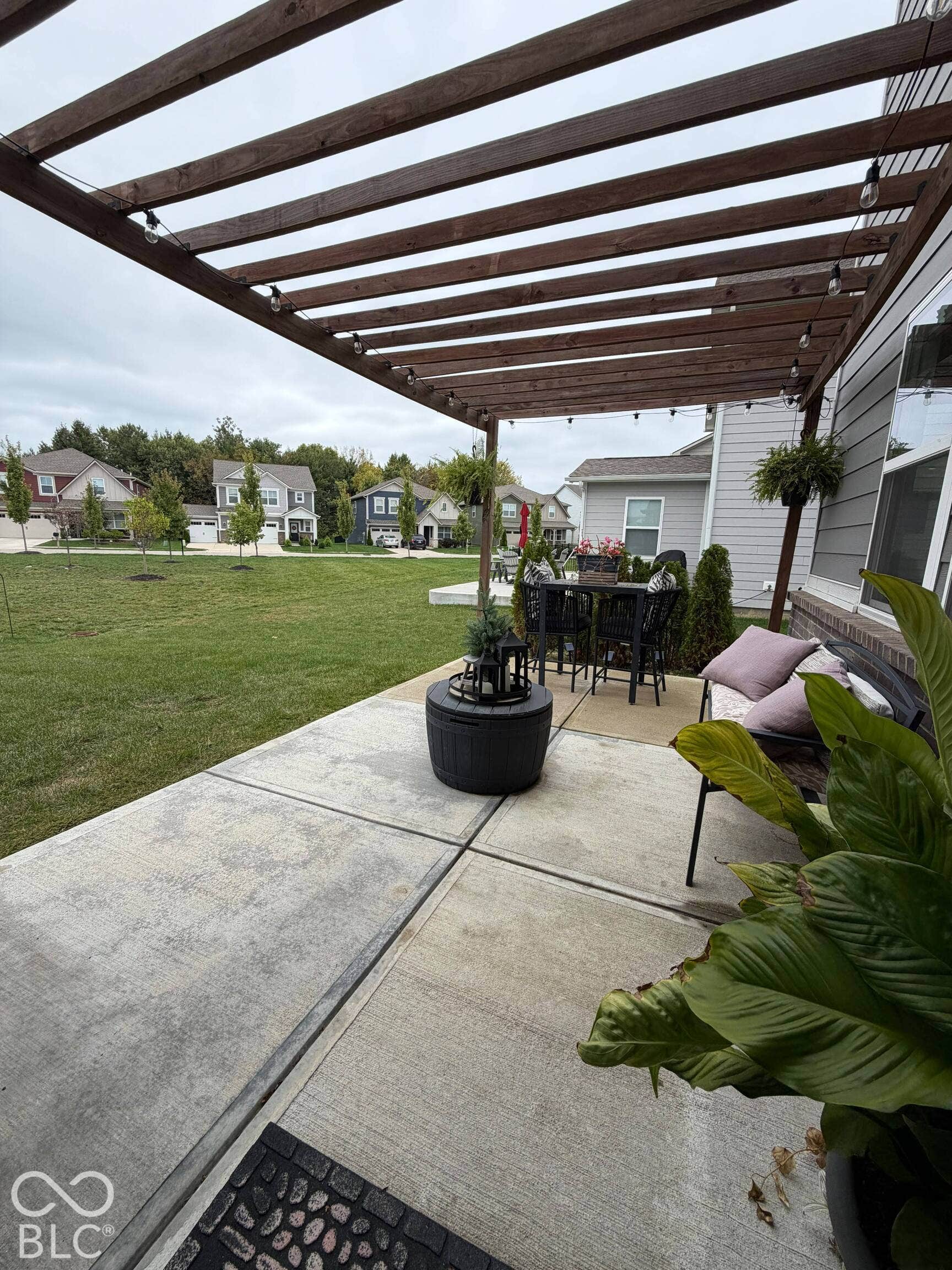 Concrete patio with a wood pergola, string lighting, and direct access to a grassy yard