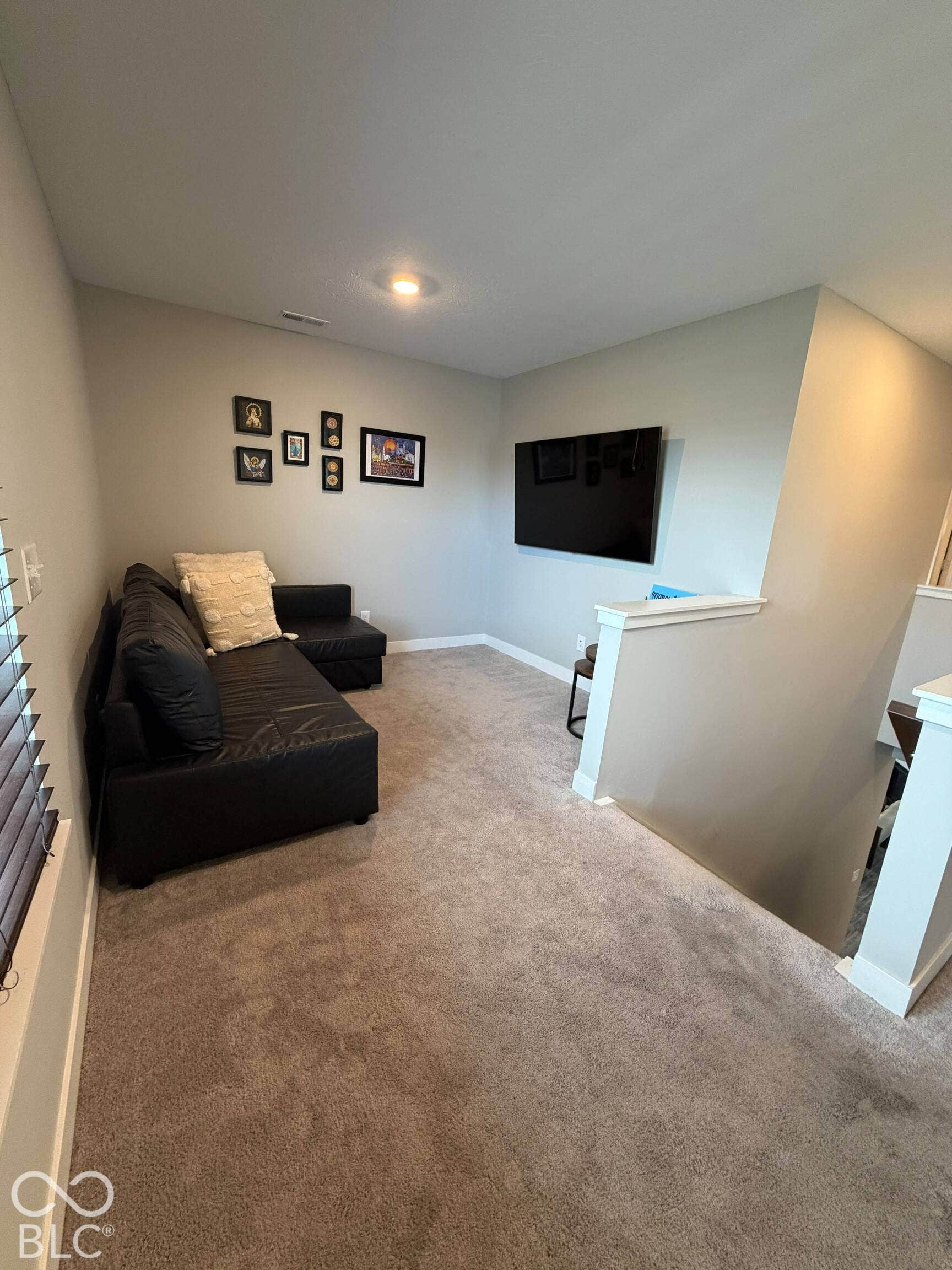 Recessed ceiling lighting illuminates a carpeted living space with a built-in wall-mounted television and window with blinds
