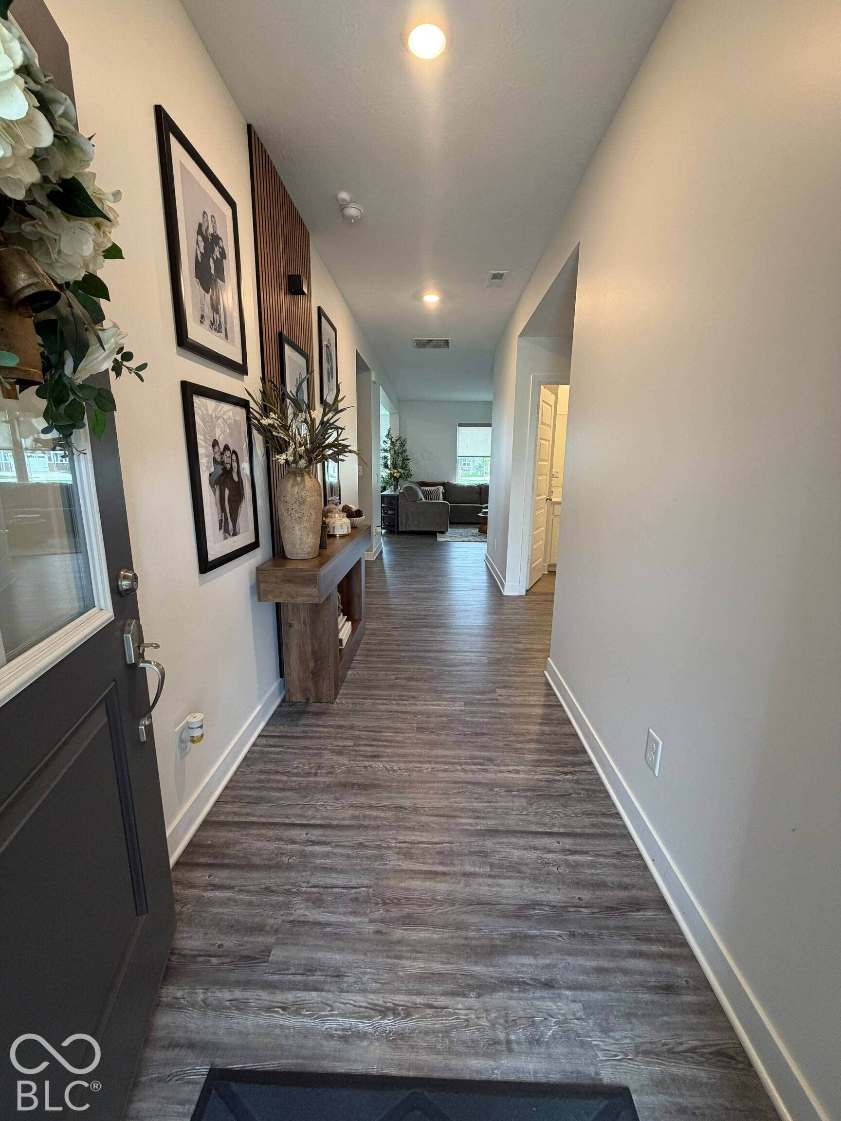 Wood-finish flooring extending through the hallway, recessed lighting, and a solid entry door with a glass inlay