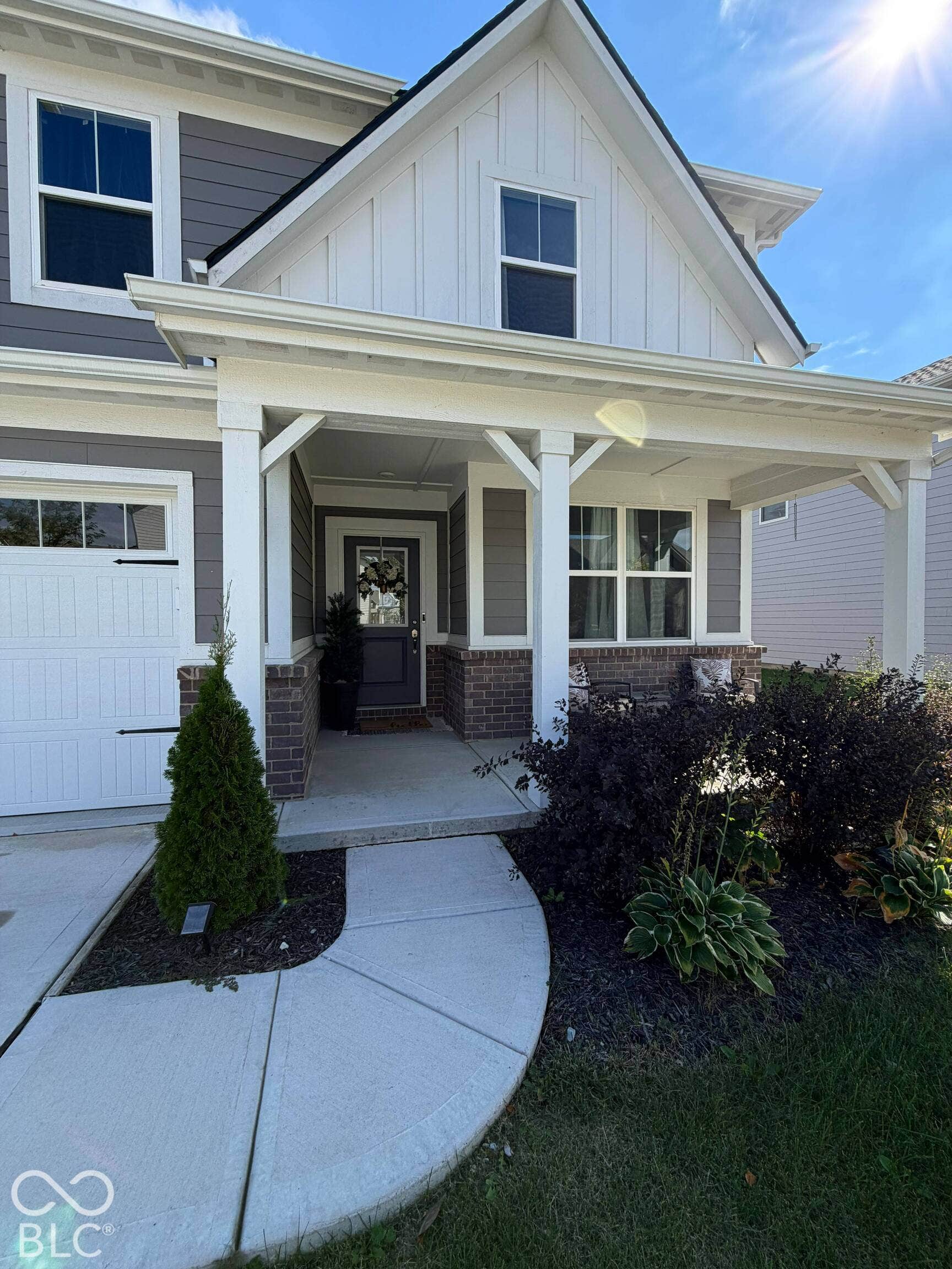 Gable roofline with white board and batten siding, gray horizontal siding, brick accents, covered entry, and a white garage door with black hardware