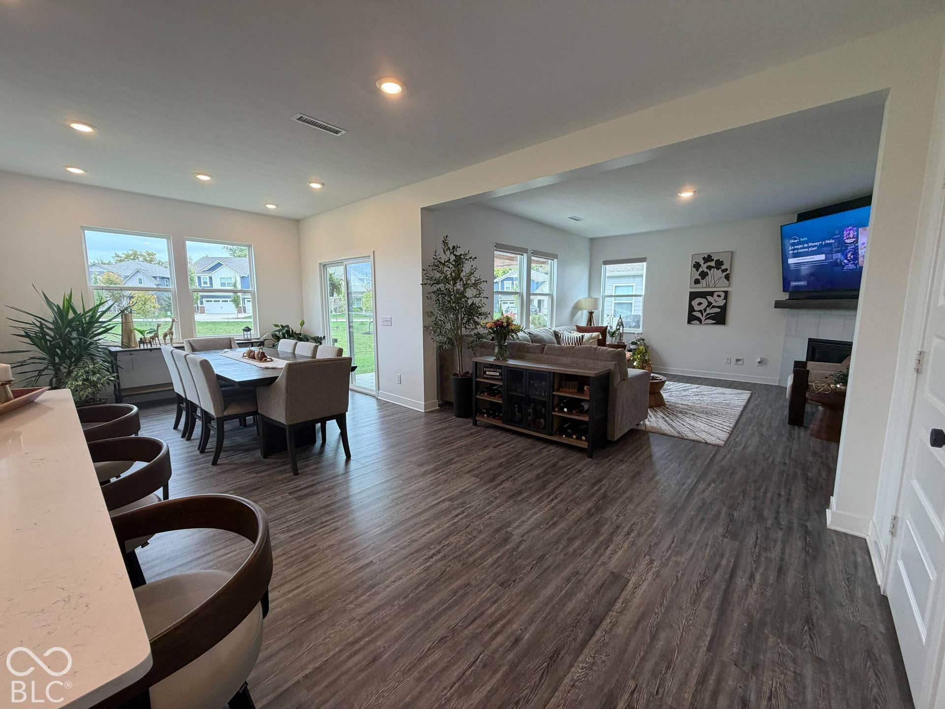 Open-concept living space with wood-finish flooring, a dining area featuring multiple windows, and a living room with a built-in fireplace