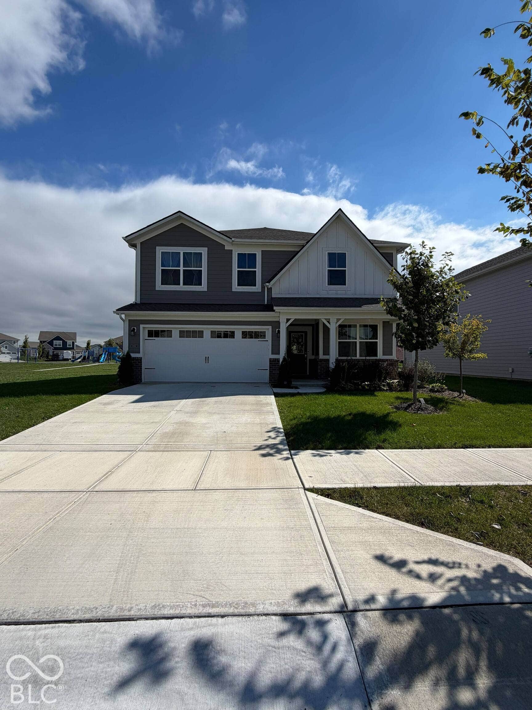 Two-story exterior with gray siding and white trim accents, prominent front gables, attached garage with white door, concrete driveway, and front lawn