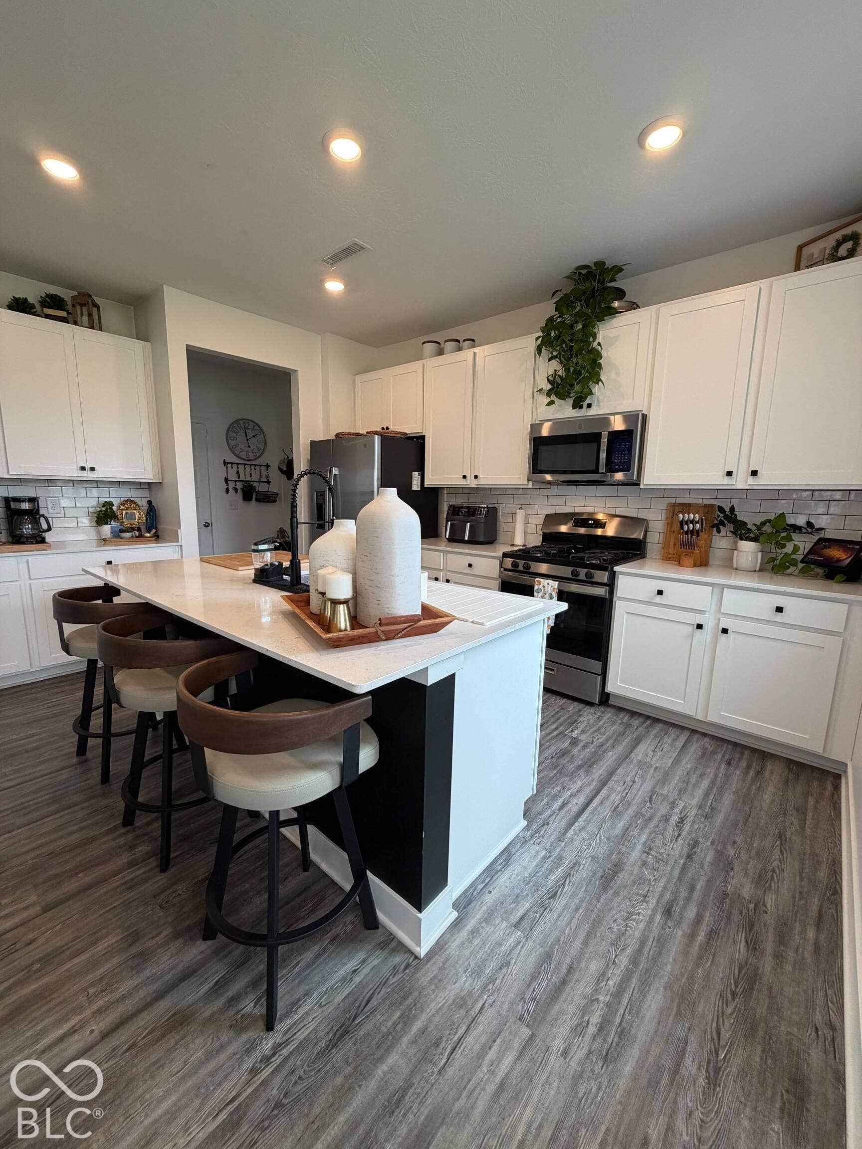 White cabinetry with black hardware, stainless steel appliances, wood-finish flooring, recessed lighting, and a kitchen island with seating