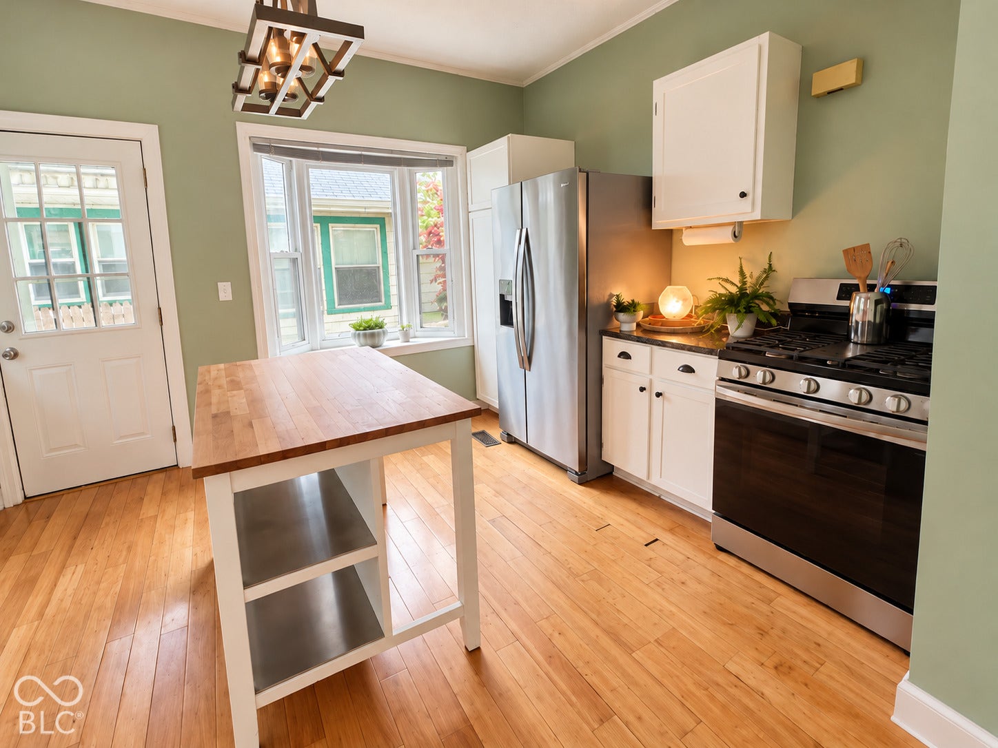 Kitchen featuring wood-finish flooring, white cabinetry, a wood-top island with shelving, stainless steel appliances, and a multi-pane bay window